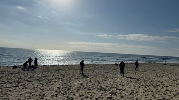 Beachgoers walk the shoreline at dusk.